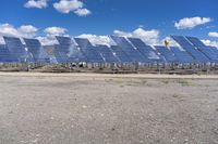 rows of solar panels sit on a paved area against a blue sky with white clouds