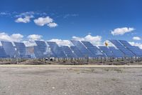 rows of solar panels sit on a paved area against a blue sky with white clouds