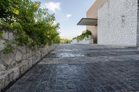 a paved walkway leading into a building with greenery on one side and a stone fence in the other