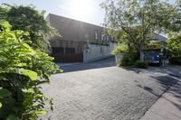 an asphalt paved driveway in front of a building with bushes and trees to the side