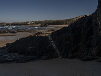 the surfer is taking advantage of the waves by himself in the distance, as others in a small group of rocks surround