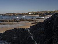 the surfer is taking advantage of the waves by himself in the distance, as others in a small group of rocks surround