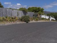 a man skateboarding in a residential area on his board with a wooden fence along the road