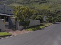 an empty street near some houses in the mountains range side view of the street, with a fenced yard and gate to it