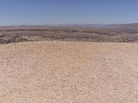 a person riding a horse along side a mountain with a dog nearby from afar, on top of a rocky hill in the middle of an arid area