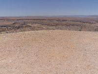 a person riding a horse along side a mountain with a dog nearby from afar, on top of a rocky hill in the middle of an arid area