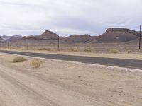 a desert landscape, including power lines, and hills with a black paved road lined with dirt