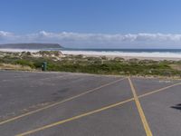 a person stands in the parking lot and is looking down at the ocean from behind him