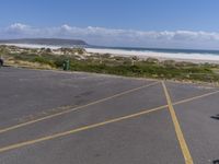 a person stands in the parking lot and is looking down at the ocean from behind him