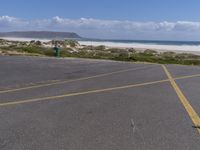 a person stands in the parking lot and is looking down at the ocean from behind him