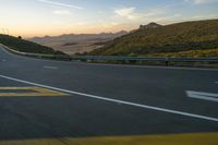 a long winding road with mountains and a mountain in the distance in the sunlight at sunset