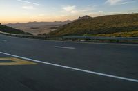 a long winding road with mountains and a mountain in the distance in the sunlight at sunset