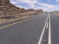 the empty street is on the rocky hill side and yellow paint shows the line of a curving road