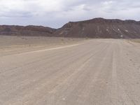 a gravel road leading through a vast barren desert area with an open sky line and mountains in the distance