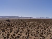 desert landscape with a fenced off dirt area and distant mountains in the background, blue sky and clouds