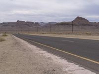 an empty road with yellow markings is in a desert area near power lines and telephone poles