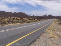 a paved road going around a mountain in the desert with mountains in the distance and telephone poles on either side