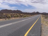 a paved road going around a mountain in the desert with mountains in the distance and telephone poles on either side