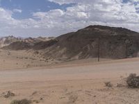 a sign is posted at the side of a desert road by a signpost and telephone lines