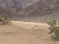 a motorcycle riding on a dirt road in front of a desert mountain range with tall mountains