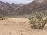 a motorcycle riding on a dirt road in front of a desert mountain range with tall mountains