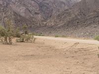 a motorcycle riding on a dirt road in front of a desert mountain range with tall mountains