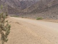 a motorcycle riding on a dirt road in front of a desert mountain range with tall mountains