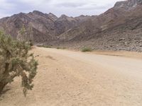 a motorcycle riding on a dirt road in front of a desert mountain range with tall mountains