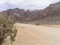 a motorcycle riding on a dirt road in front of a desert mountain range with tall mountains