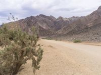 a motorcycle riding on a dirt road in front of a desert mountain range with tall mountains