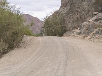 a motorcycle rides down the road near some rocks and trees, in between two mountains