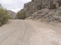 a motorcycle rides down the road near some rocks and trees, in between two mountains