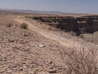 a man riding on top of a dirt field next to a canyon and a blue sky