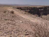 a man riding on top of a dirt field next to a canyon and a blue sky