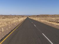 a long empty highway runs through a dry and barren desert landscape on a sunny day