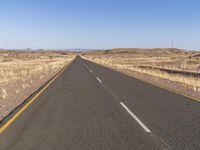 a long empty highway runs through a dry and barren desert landscape on a sunny day