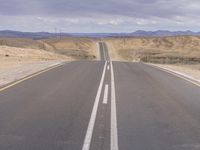 an empty road in the middle of a desert landscape with two lines painted along it