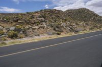 a motorcycle riding along a winding road next to mountains in the day time and blue skies