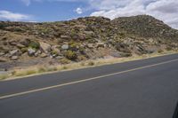 a motorcycle riding along a winding road next to mountains in the day time and blue skies