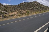 a motorcycle riding along a winding road next to mountains in the day time and blue skies