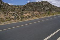 a motorcycle riding along a winding road next to mountains in the day time and blue skies