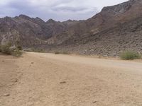 a person that is riding a horse across a dirt field on a road between mountains