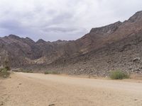 a person that is riding a horse across a dirt field on a road between mountains