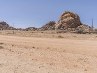 an orange motorcycle is driving down a dirt road past large rock formation in the distance