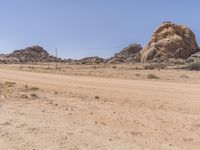 an orange motorcycle is driving down a dirt road past large rock formation in the distance