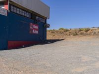 the red and blue building is set in dirt area and it has street signs on top of it