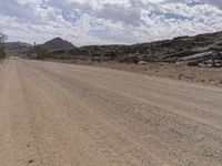 a long dirt road lined with rocks and desert in the desert under a partly cloudy sky