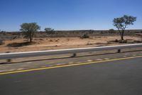 a view of a bridge from the side of a bus window, looking out to a dirt field with a rail road