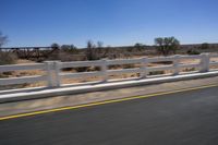 a view of a bridge from the side of a bus window, looking out to a dirt field with a rail road