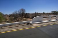 a view of a bridge from the side of a bus window, looking out to a dirt field with a rail road